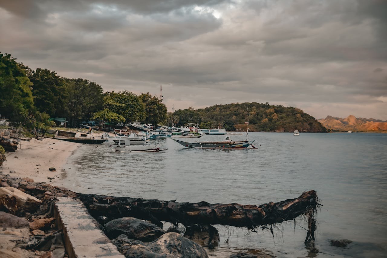 Capture of a serene tropical beach with traditional boats moored along the shore on a cloudy day.